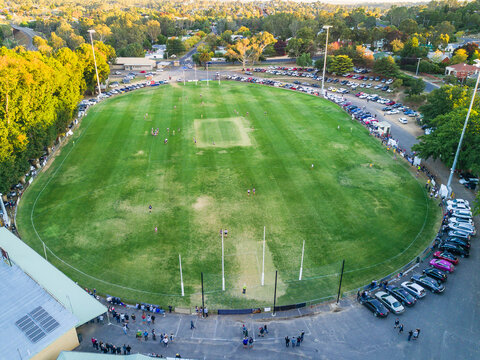 Aerial view of game of football being played on an oval surrounded by cars