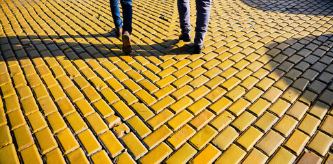 Walking men on lively yellow cobblestone and pedestrian way in Sofia Bulgaria. Men wearing brown boot staying and their shadows bottom.
