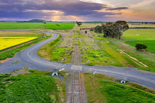 Aerial view of a country road winding through a railway crossing at sunset