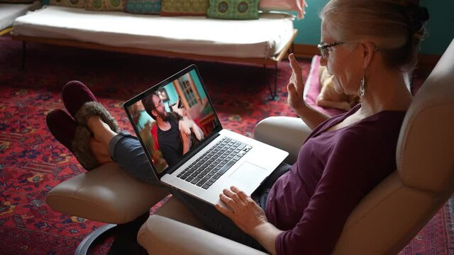 Woman smiling with her feet with slippers up while having video chat with man with Husky dog on her laptop computer in living room. Concept of remote social distancing.