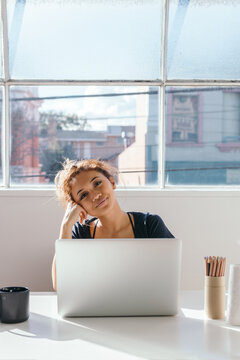 Woman looking content at camera from behind her laptop in a beautiful studio