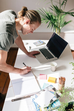 Blond young man writing in a notebook on a desk from above