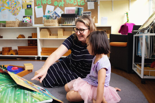 Happy multicultural teacher and child reading a book in kindergarten