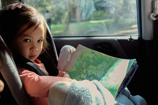 Young girl in car seat reading map on road trip