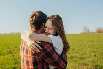 Happy couple outdoors is relaxing on the green field. They hugging each other.