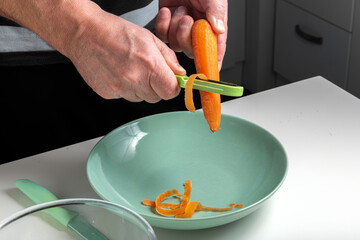 A man in the kitchen peels carrots Home cooking vegetarianism Healthy food Home food Hands