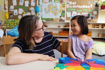 Happy multicultural teacher and child with wooden blocks puzzles in kindergarten