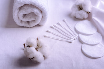 Obraz na płótnie Canvas Clean towels, cotton pads and sticks and cotton flowers on table. Natural cotton fabric texture