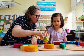 Multicultural teacher and child playing wooden blocks puzzles in kindergarten