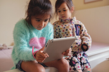 Multicultural kids using tablet in bedroom