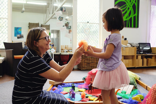 Happy multicultural teacher and child with wooden blocks puzzles in kindergarten