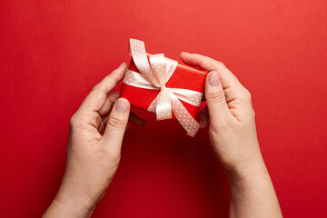 Gift box with ribbon in female hands on red background