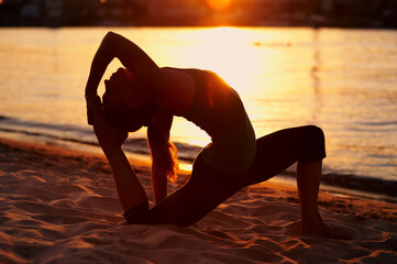 Silhouette of a young blonde woman practicing yoga at sunset near the river.