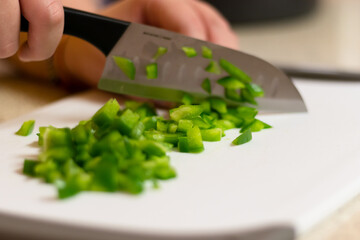 A fresh green bell pepper being chopped in to diced pieces on a white cutting board with a knife.