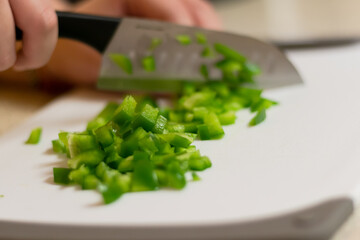 A fresh green bell pepper being chopped in to diced pieces on a white cutting board with a knife.