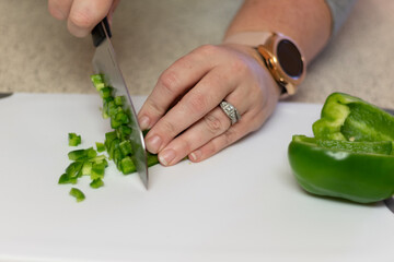 A fresh green bell pepper being chopped in to diced pieces on a white cutting board with a knife.
