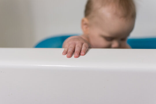 7 month old baby sitting upright in blue infant bath tub; hand grasps edge of bathtub