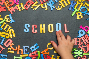 Child's hand laid out the word school from multicolored plastic letters