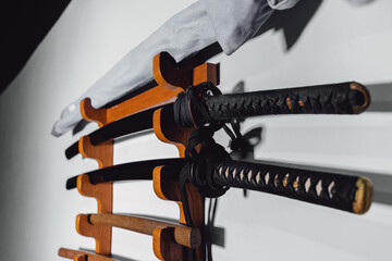 Special stand on the white wall for training swords made of oak wood and iron. Traditional Japanese training weapons for different martial arts disciplines.