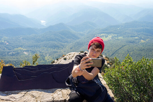 Young male with wool red hat sitting against mountain taking a selfie
