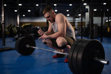 Sportsman sitting near barbell in gym