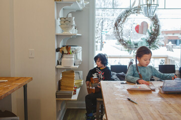Two children sit together in kitchen creating music and art by window