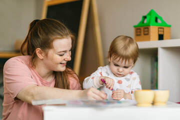 Early childhood learning. Mother and child play with wooden beads and cups, teaching colors and developing fine motor skills