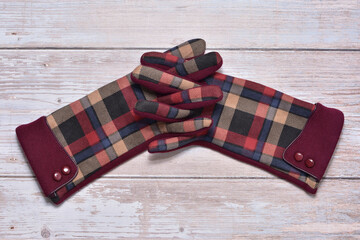 Vintage colorful pattern gloves entwined in fingers on wooden background.