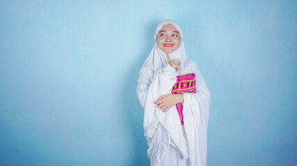 asian woman wearing muslim hijab scarf mukena thinking, imagination, question, having idea isolated on blue background in studio. ramadan concept