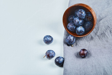 Ripe plums in a bowl with gray tablecloth on white table