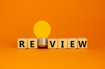 Review symbol. Wooden cubes with word 'review'. Yellow light bulb. Beautiful orange background....