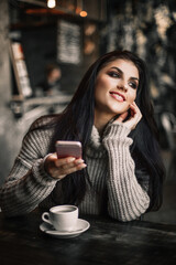 Woman using phone and drinking coffee in a cafe.