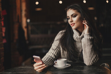 Woman using phone and drinking coffee in a cafe.