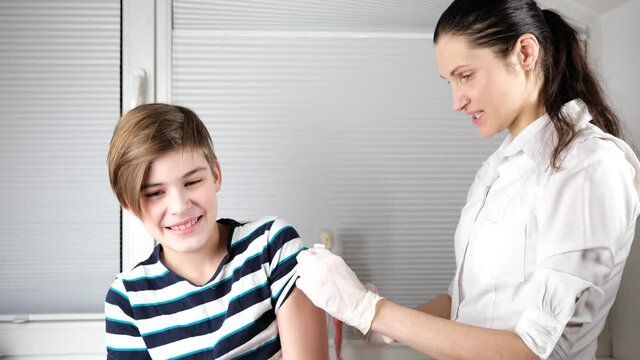 doctor in gloves disinfecting the boy arm skin by cotton before giving a injection vaccine to patient