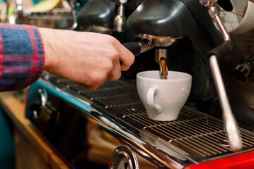 Male hands of the barista near the coffee machine. Barista makes cappuccino with a coffee machine. The coffee from the machine is poured into a classic white cup. Popular hot drinks. Men's work. 