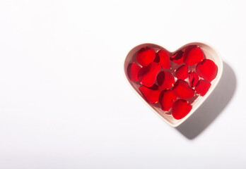 White heart shaped bowl with red rose petals on the water surface