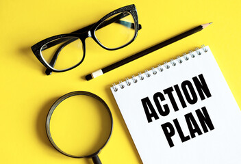 ACTION PLAN text written on a notebook with glasses, magnifying glass and pencil.