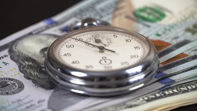 The stopwatch is on top of the 100 dollars bills and the hand is ticking. The concept of sales, discounts and investments in stocks and businesses.