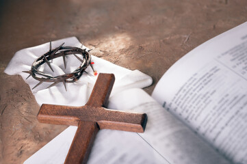 Crown of thorns and Wooden cross over open bible background with copy space for inscription. ...