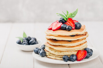 Classic american pancakes with fresh berry on white wood background. Summer homemade breakfast.