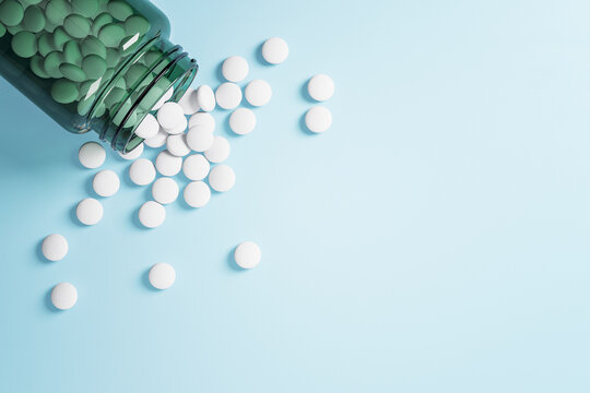 White pills spilled out of bottle on blue table.