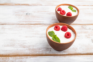 Yogurt with raspberry in clay cups on white wooden background. Side view, copy space.
