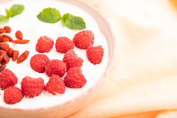 Yogurt with raspberry and goji berries in ceramic bowl on white concrete background. Side view, selective focus.
