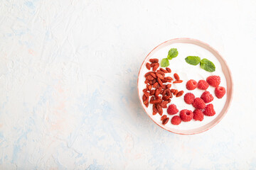 Yogurt with raspberry and goji berries in ceramic bowl on white concrete background. top view, copy space.