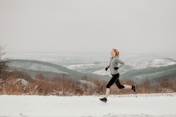 Sportswoman sprinting fast in nature on snowy path at winter. Healthy lifestyle, winter fitness, cold weather