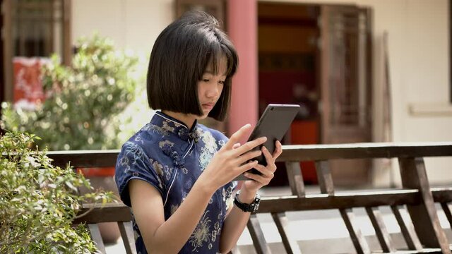 Asian girl wearing Chinese dress or Qi Pao in Chinese new year festival using tablet.