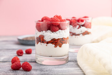 Yogurt with raspberry, goji berries and chia seeds in glass on gray wooden background. Side view, selective focus.