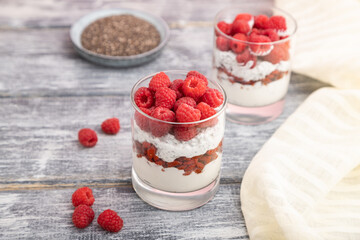 Yogurt with raspberry, goji berries and chia seeds in glass on gray wooden background. Side view, selective focus.