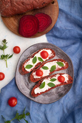 Red beet bread sandwiches with cream cheese and tomatoes on white concrete background. top view, close up.