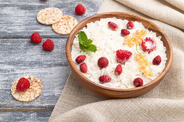 Rice flakes porridge with milk and strawberry in wooden bowl on gray wooden background. Side view.